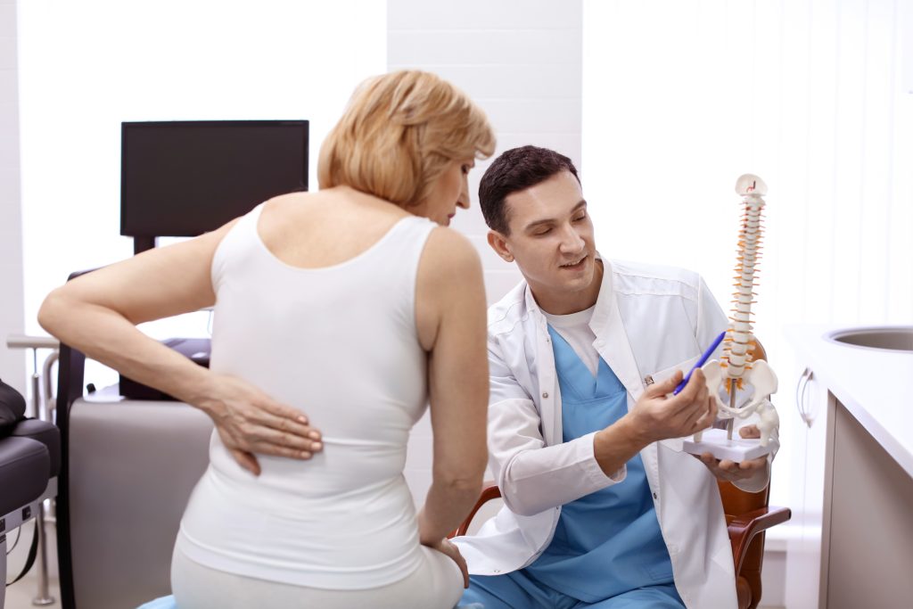 Orthopäde zeigt einem Patienten im Krankenhaus ein Wirbelsäulenmodell